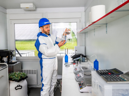 man met helm en pak in lab om fosfaat uit slib te halen
