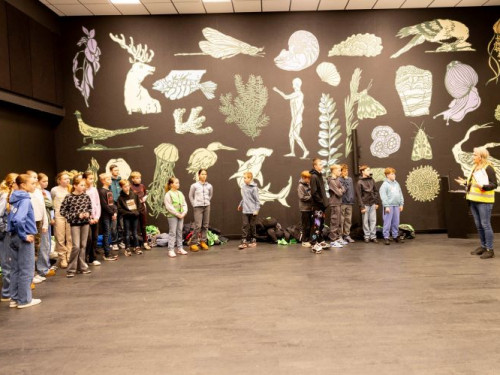 kinderen staan in zaal met illustraties op de wanden.