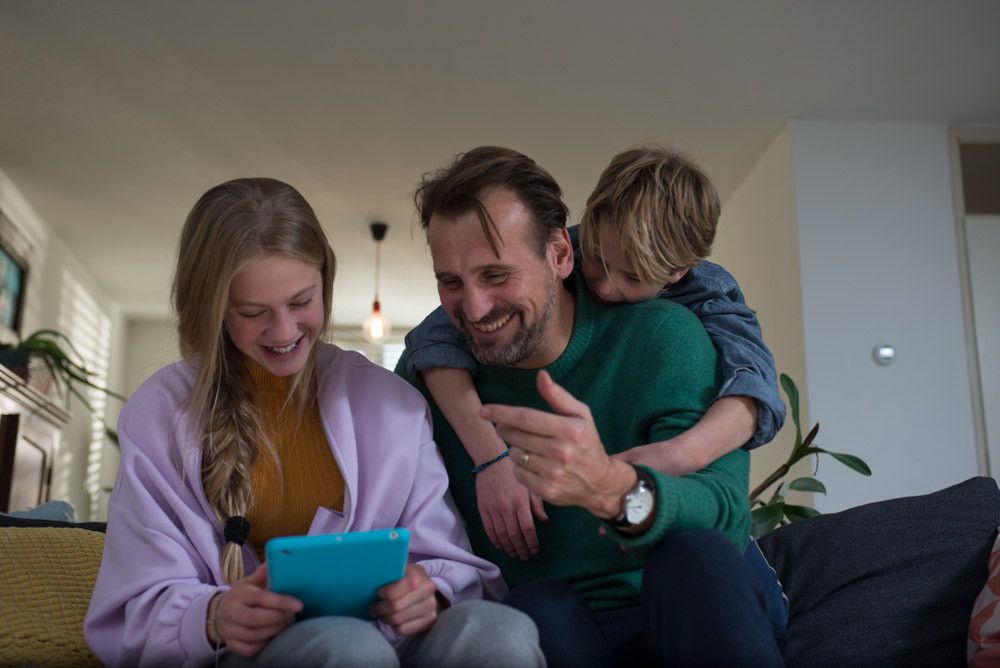 vader en 2 kinderen zitten op de bank en kijken lachend naar een tablet.